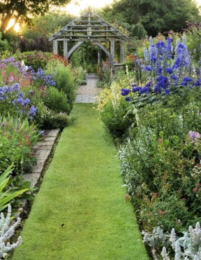 Wollerton Gardens In England with purple, blue, white and red flowers in bloom on either side of a grass pathway